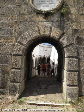 Portico e portão da fortaleza construída em cantaria ou pedra talhada. Sobre o portão a placa em homenagem a D.Pedro II e ao fundo o corredor externo das baterias.